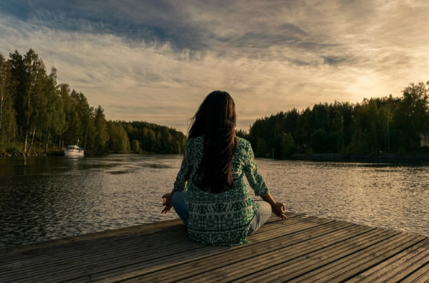 Femeie care practica meditatia pe malul unui lac