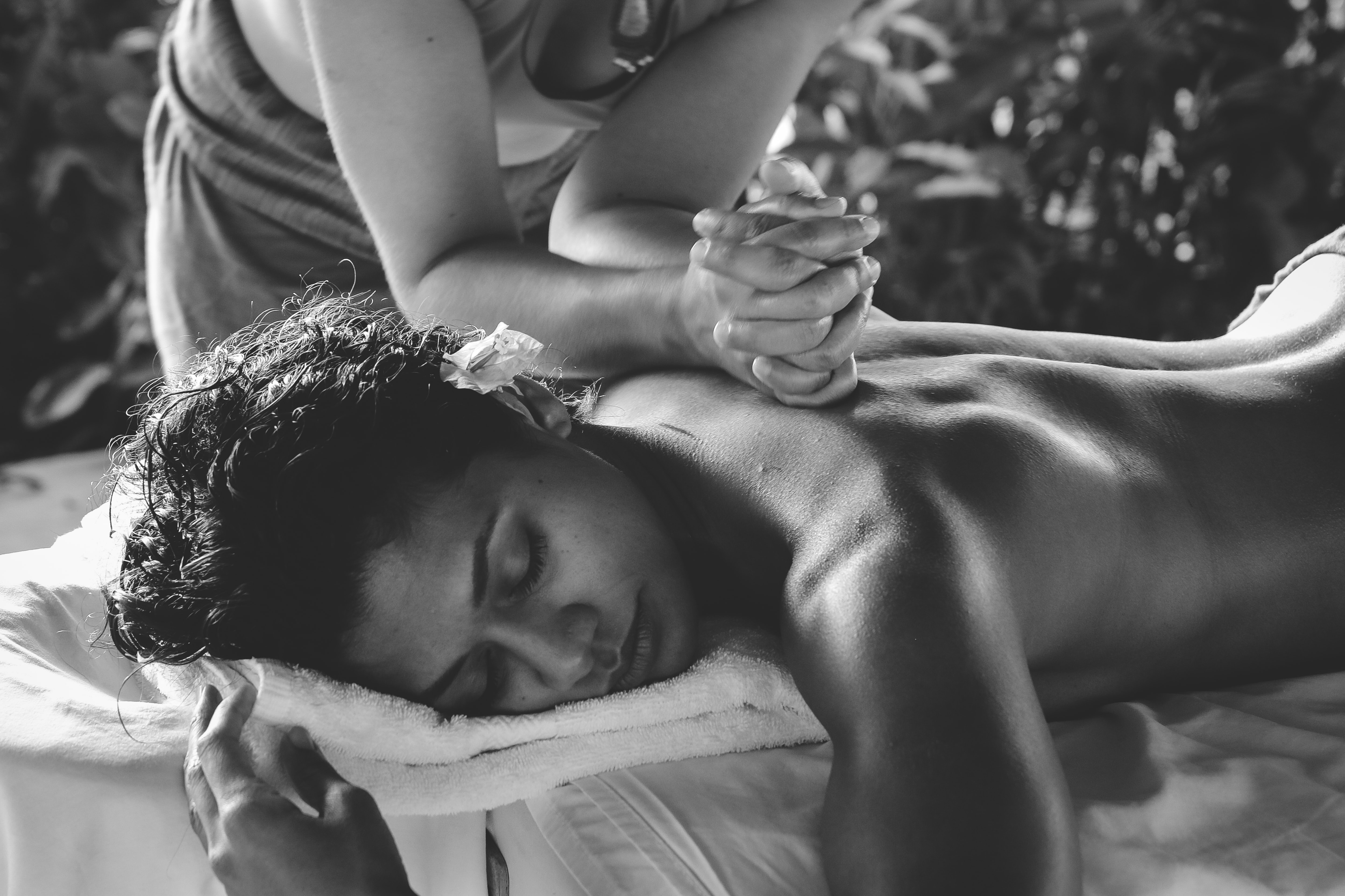 Imagine alb negru cu o femeie careia i se face un masaj in zona cervicala, bratele terapeutului fiind vizibile pe spatele ei.