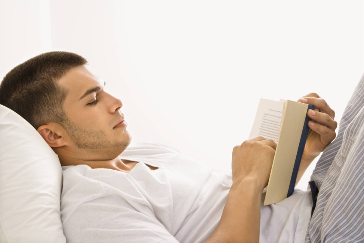 Bărbat citind relaxat o carte stând în pat