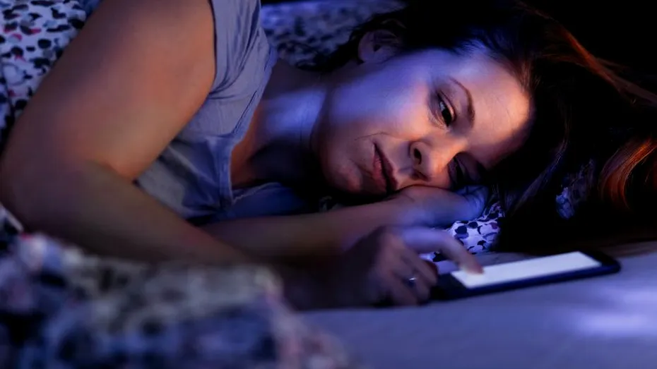 Femeie pornind telefonul mobil, noaptea, stând în pat