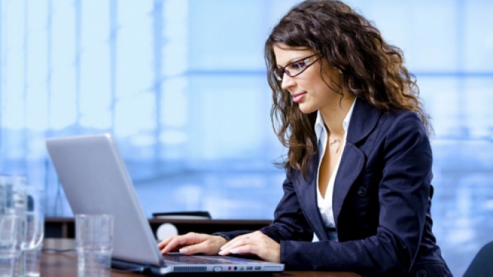 Femeie lucrând la laptop într-un office, la un birou