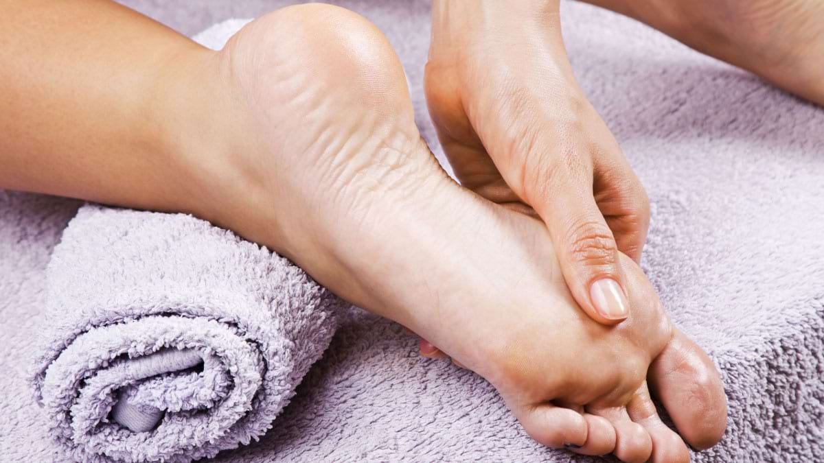 Mâna unui terapeut efectuând un masaj reflexoterapeutic pe talpa piciorului unei femei
