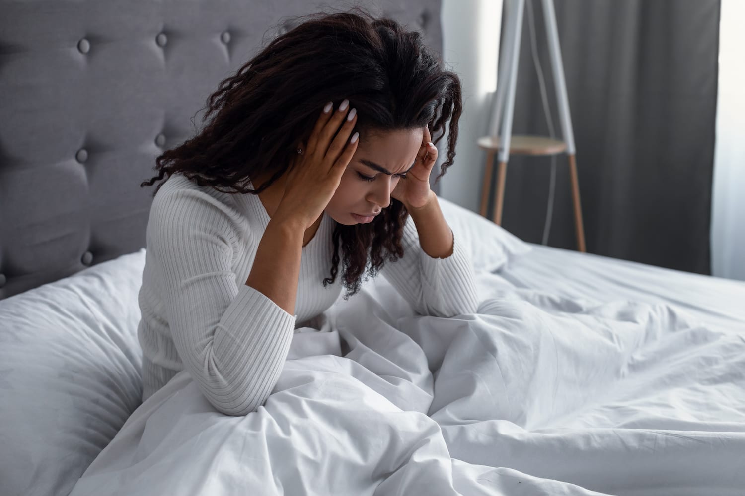 Femeie mulatră strând în pat, acuzând o durere de cap
