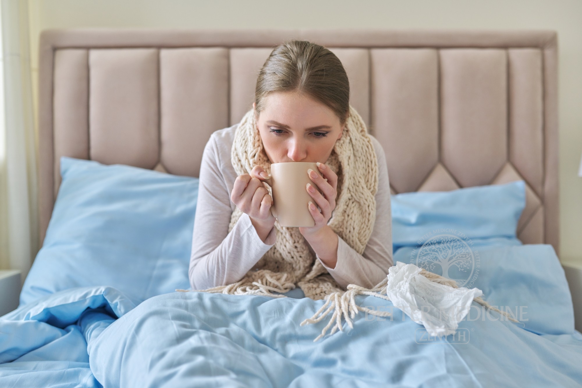 Femeie stând înfofolită în pat, bolnavă, servind un o ceașcă de ceai